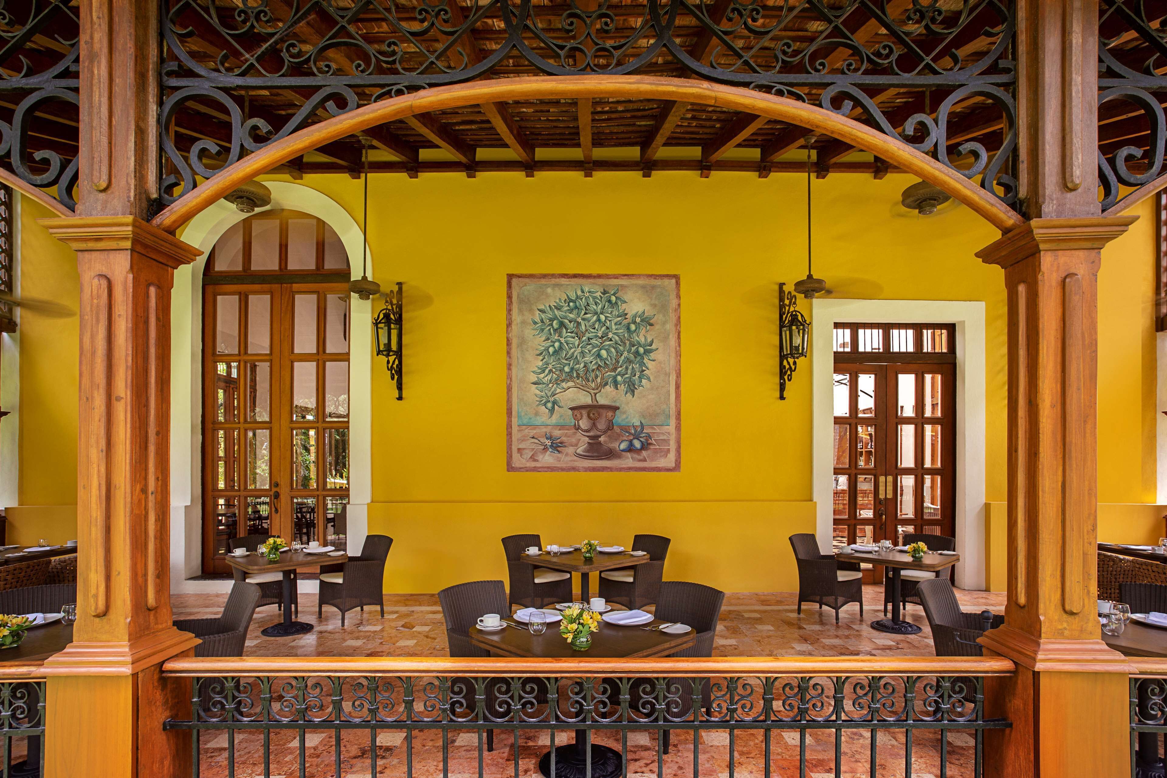 A dining area with a table set for four, surrounded by chairs, with a yellow wall and a painting above.