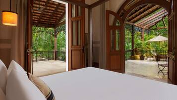A hotel room with a large bed, wooden doors leading to a balcony with a view of lush greenery.