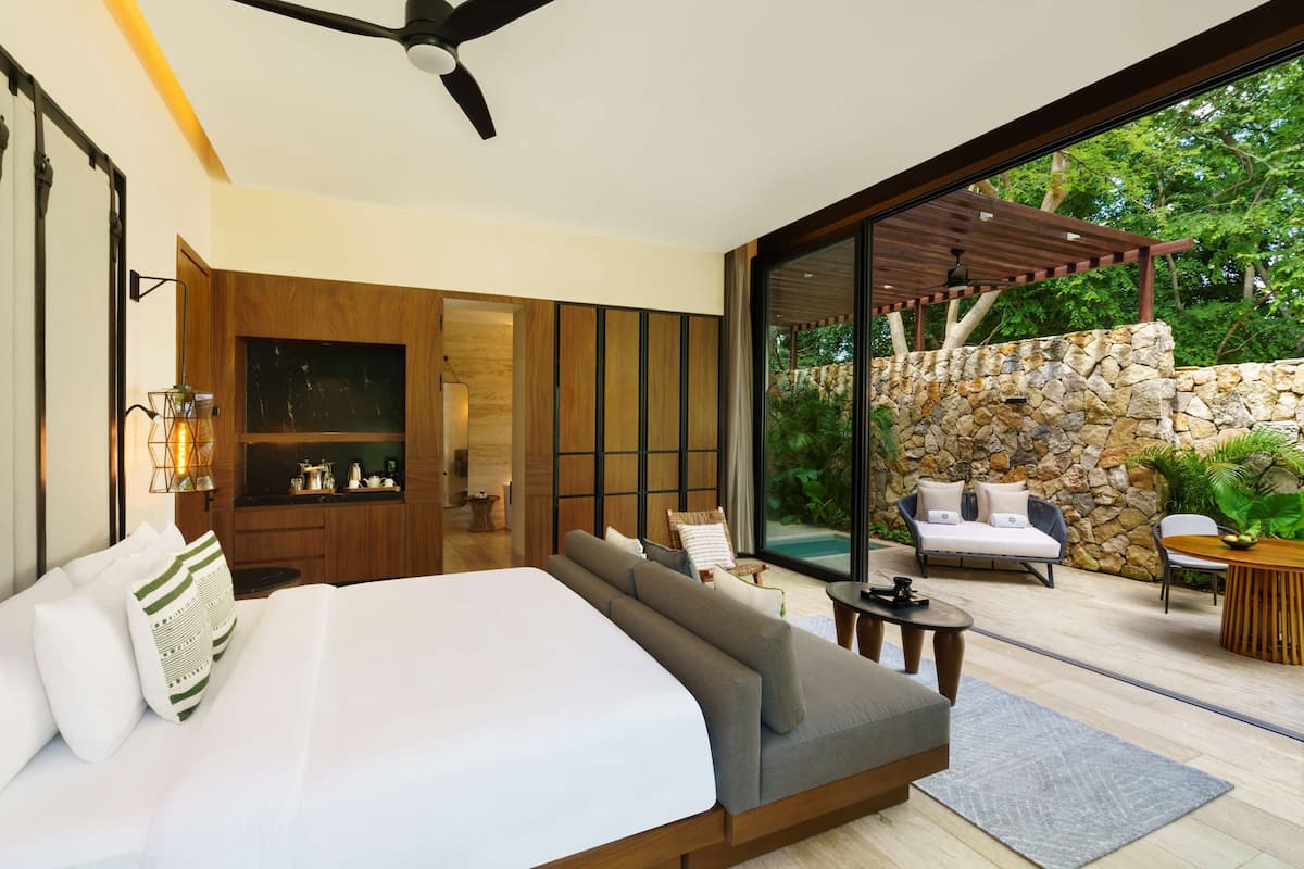 A modern bedroom with a large bed, a wooden wardrobe, a built-in TV, and a stone wall.