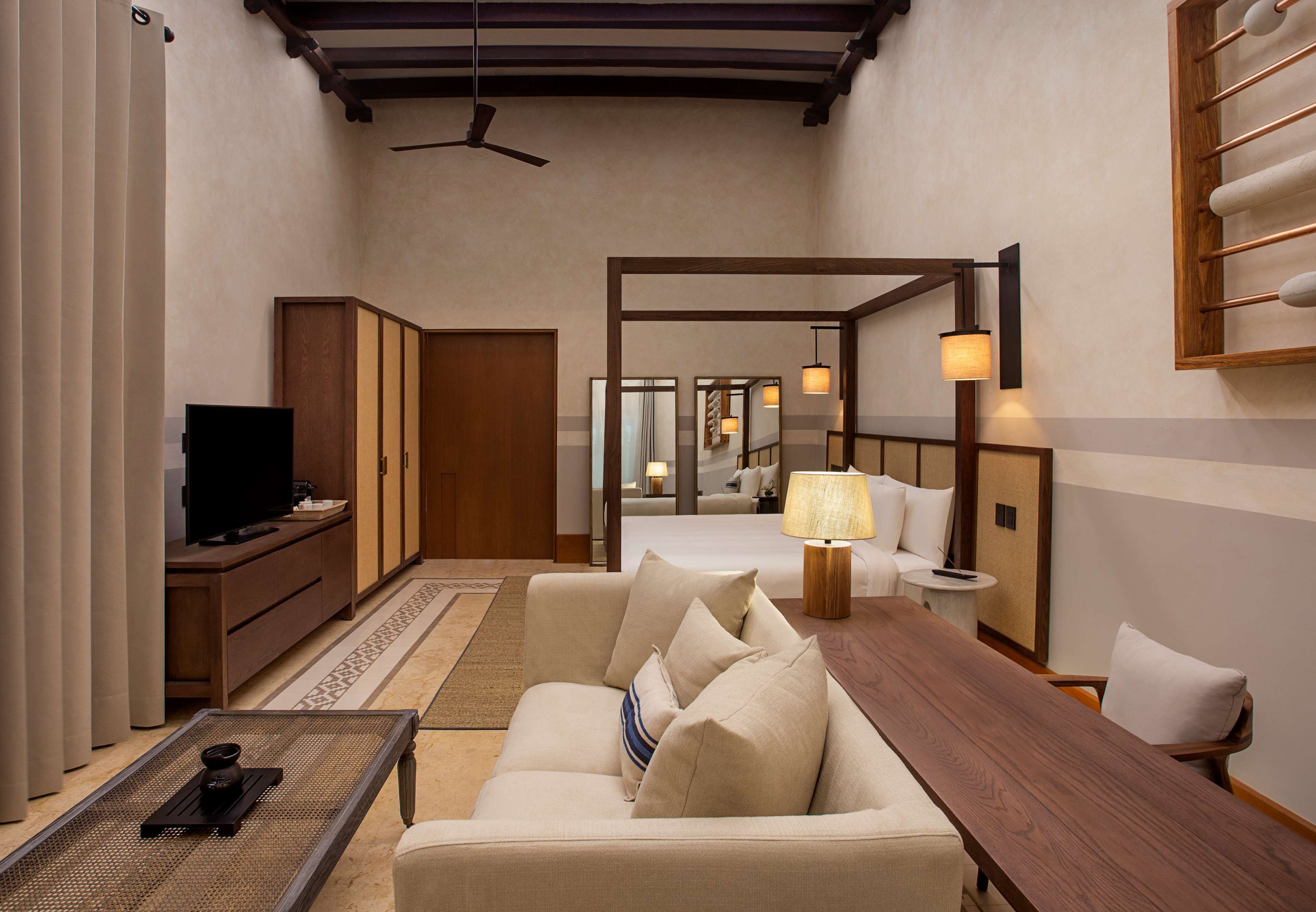 A hotel room with a sofa, a wooden coffee table, a TV, a lamp, and a mirror.
