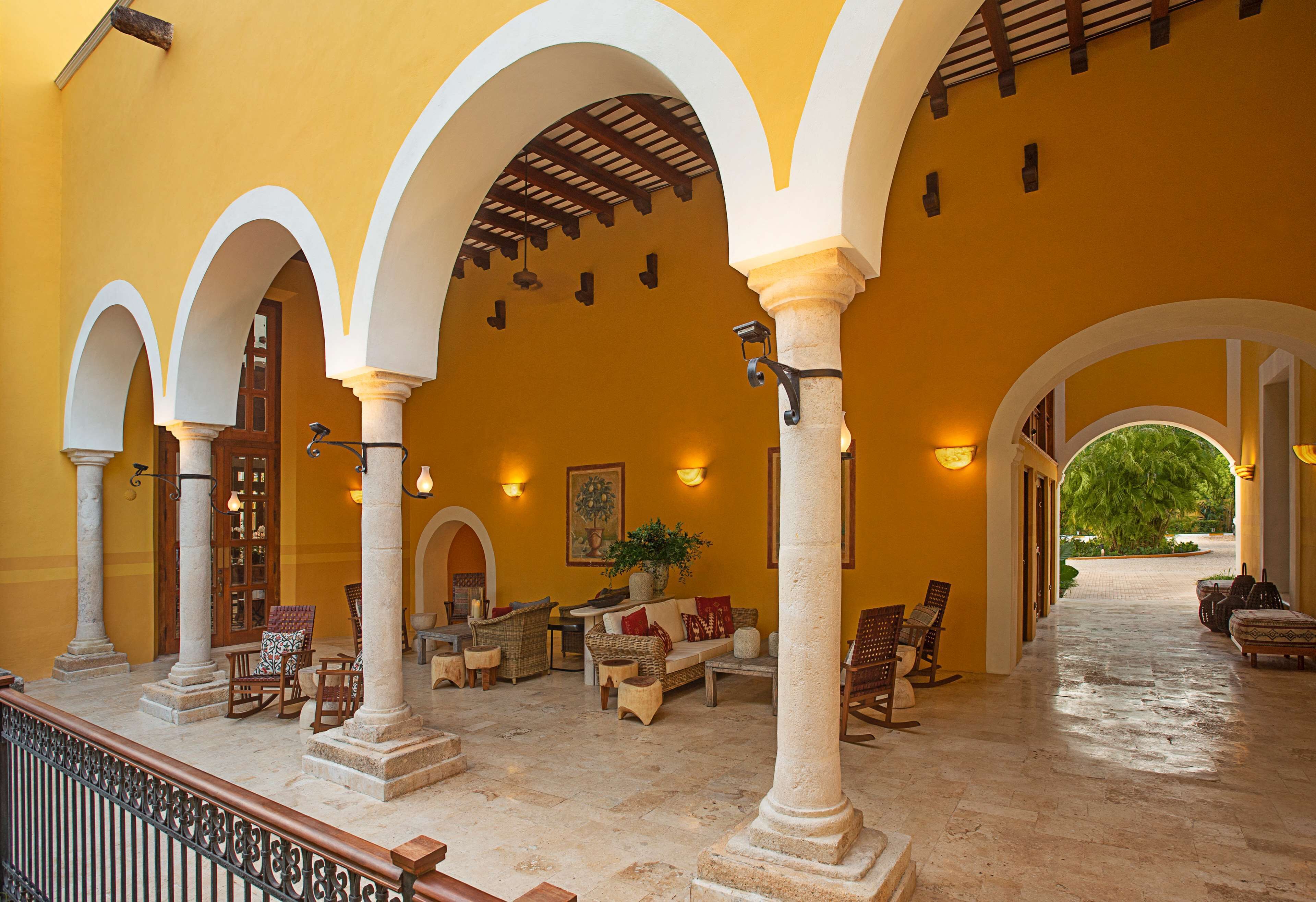 A covered outdoor area with multiple arches, seating arrangements, and a pathway leading to a green area.