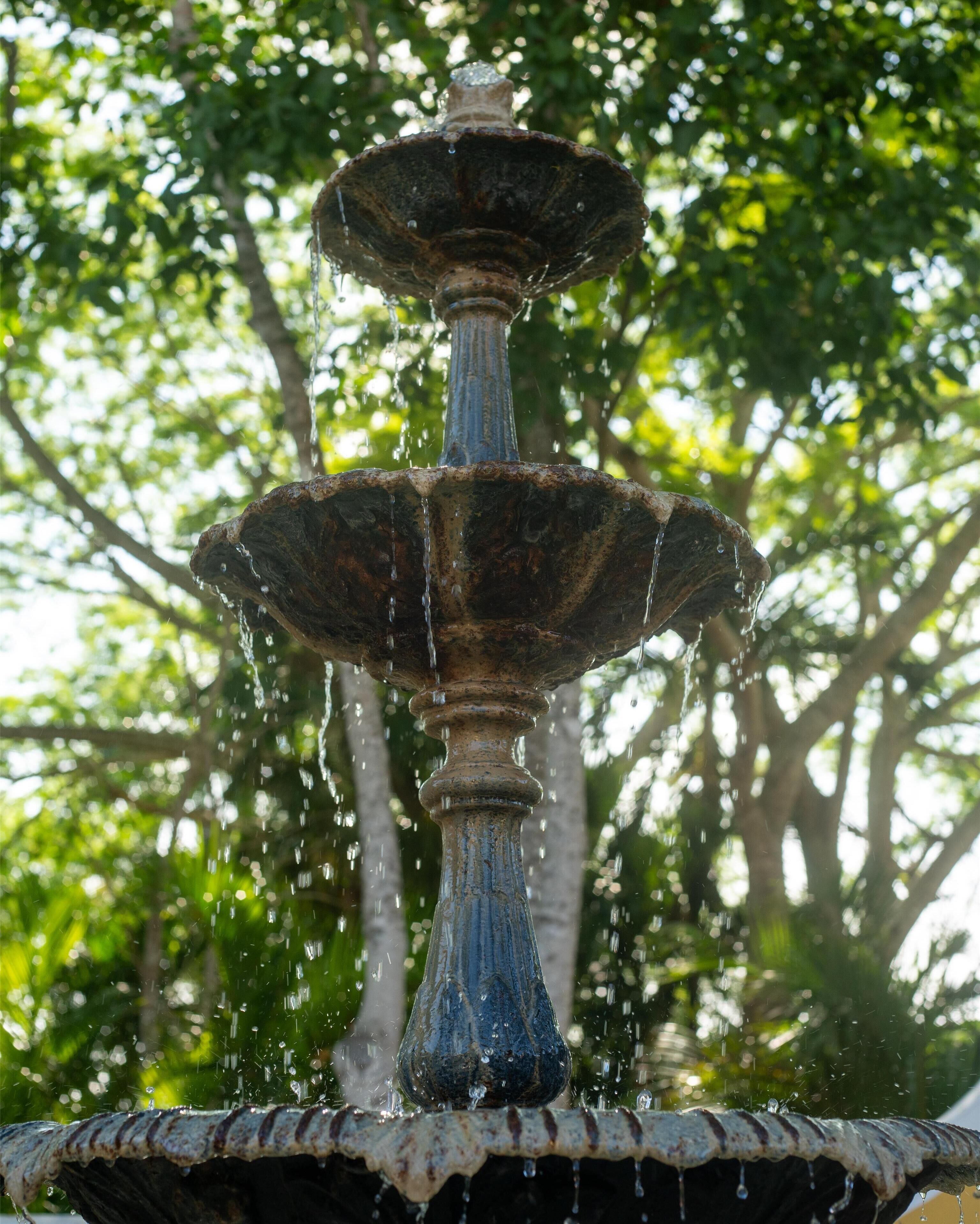 A multi-tiered fountain with water cascading down its structure, set against a backdrop of trees.