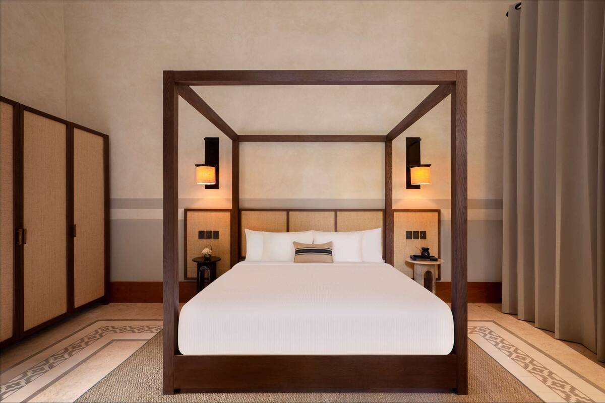 A four-poster bed with a wooden frame, white linens, and two bedside lamps.