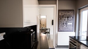 A modern kitchen with a black countertop, white cabinets, and a dining area with chairs. - Stay Comfortable- New and stylish holiday home (Burslem)