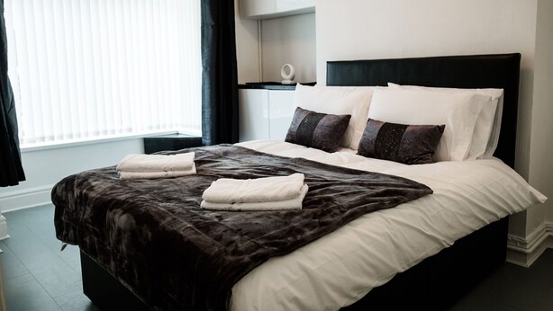 A neatly made bed with a dark headboard, white pillows, and a folded white towel. - Stay Comfortable- New and stylish holiday home (Burslem)
