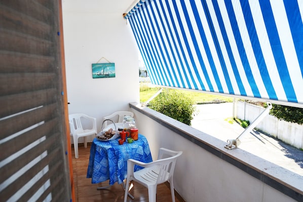 A balcony with a striped awning, a table with chairs, and a hanging picture.