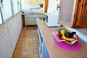A compact kitchen with a microwave, sink, and stove. A fruit bowl is on the counter.