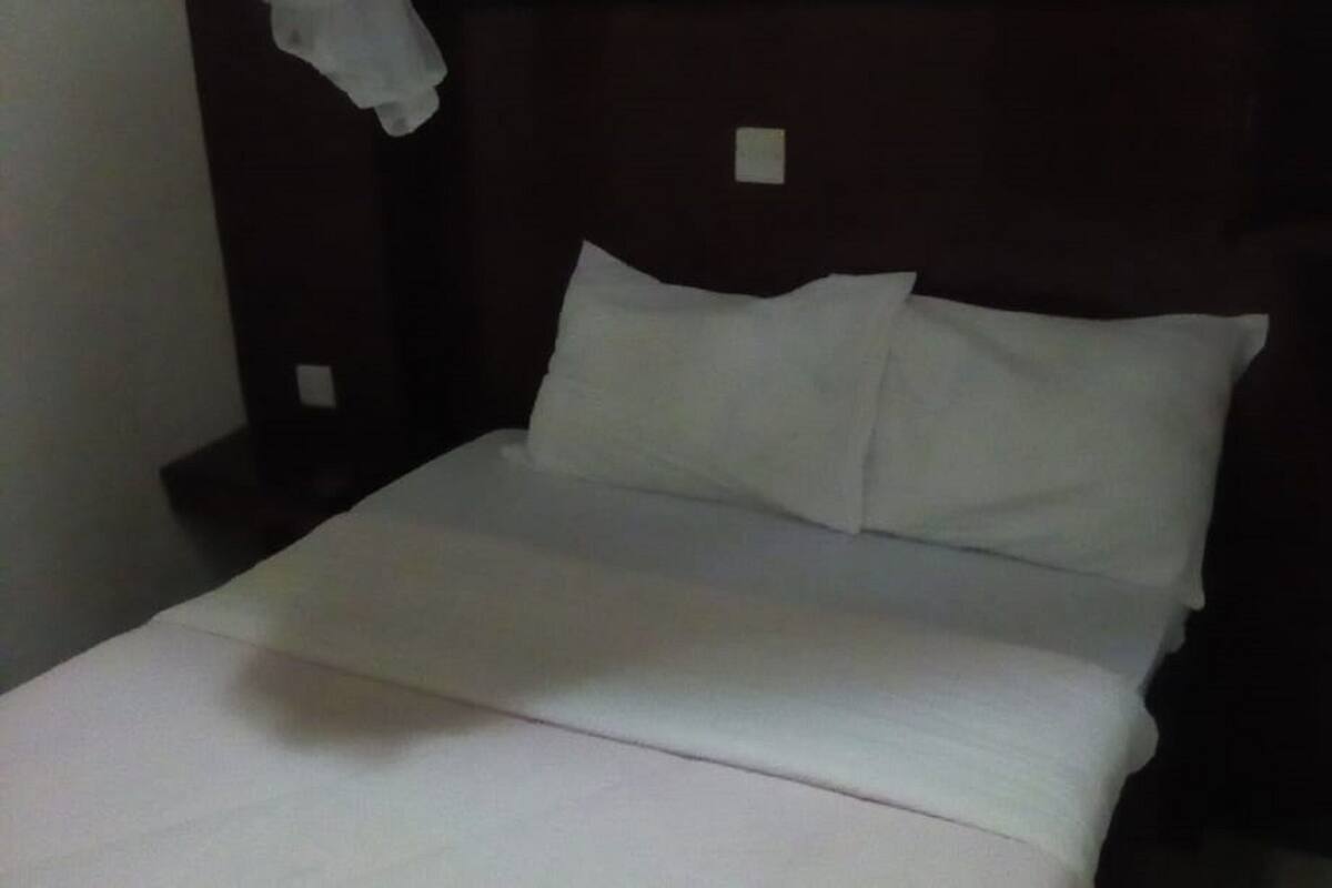 Una cama bien tendida con sábanas blancas en una habitación con poca luz.