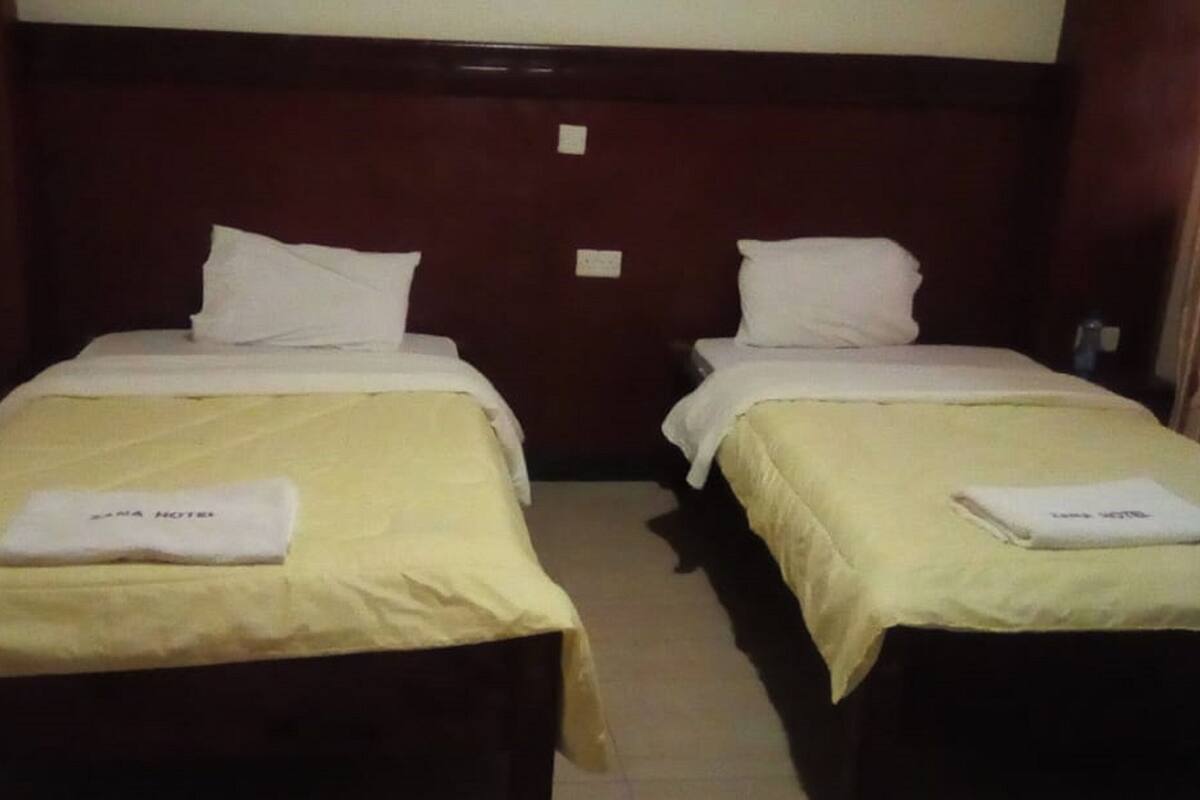 Una habitación de hotel con dos camas individuales, cada una con una almohada blanca y una toalla doblada sobre la cama.