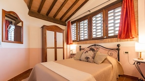 A neatly made bed with a quilt, a wooden headboard, and a window with shutters. - Apartment in farmhouse, Girasole 6+1, Volterra area, San Gimignano, Pisa (Montelopio di Peccioli)