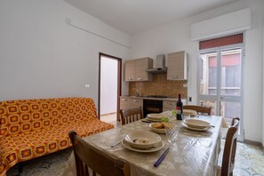 Un comedor con una mesa dispuesta para dos personas, un sofá y una cocina al fondo.
