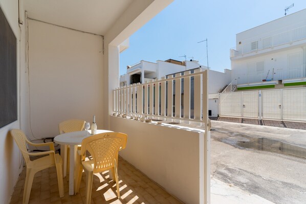 A balcony with a table and chairs, a view of the street, and a building with balconies.
