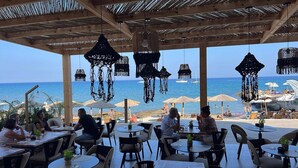 An outdoor seating area with tables and chairs, overlooking the sea with umbrellas and hanging decorations. - Silver Beach Hotel (Kos)