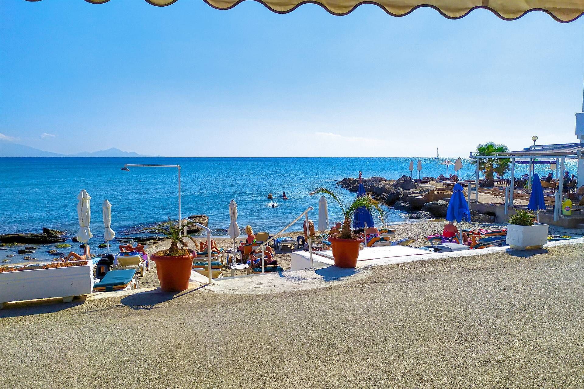 Zona sulla spiaggia con lettini, ombrelloni e piante in vaso.