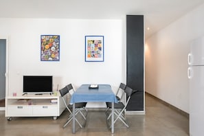 A modern living space with a dining table, chairs, a TV on a white cabinet, and two framed posters on the wall.