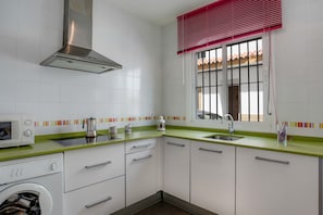A kitchen with a washing machine, a microwave, a stainless steel range hood, a window with bars, and a green countertop.