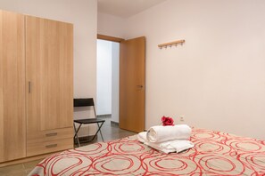 A bedroom with a bed, a wooden wardrobe, a chair, and a door leading to another room.