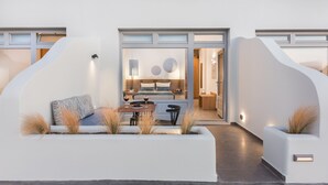 A modern outdoor seating area with a table and chairs, a bench, and decorative plants. - Volcanic Arc Suites (Santorini)