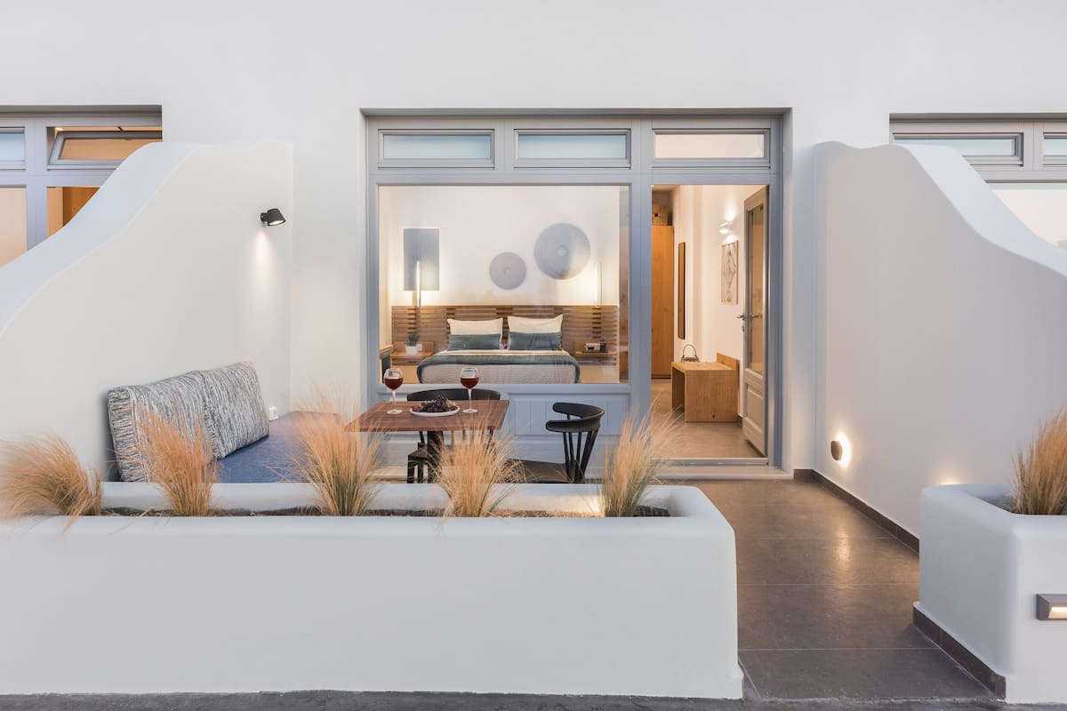 Uma área de estar moderna ao ar livre, com mesa, cadeiras, um banco e plantas decorativas.