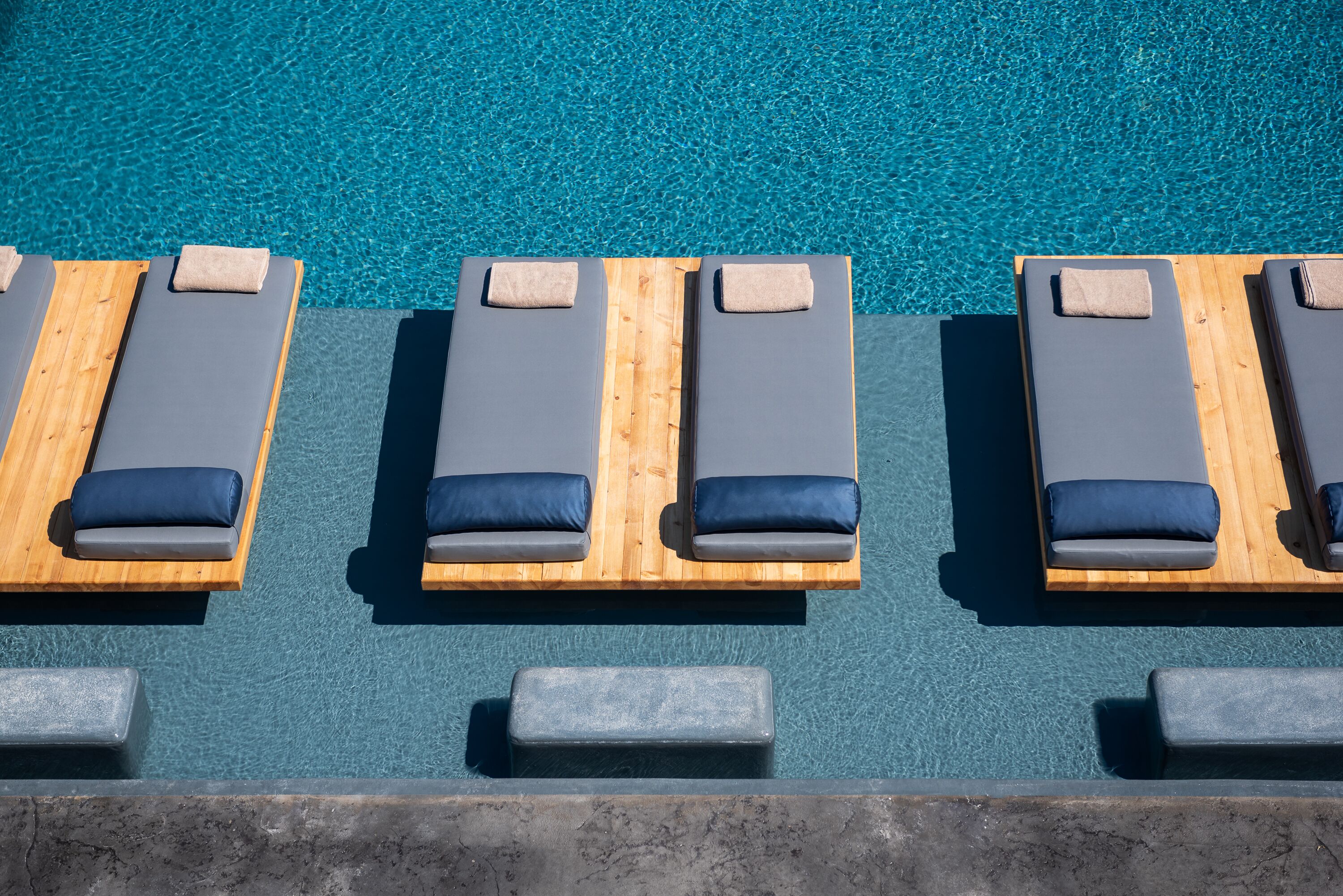 Zona de piscina con tumbonas y bancos de madera, cada uno con cojín.