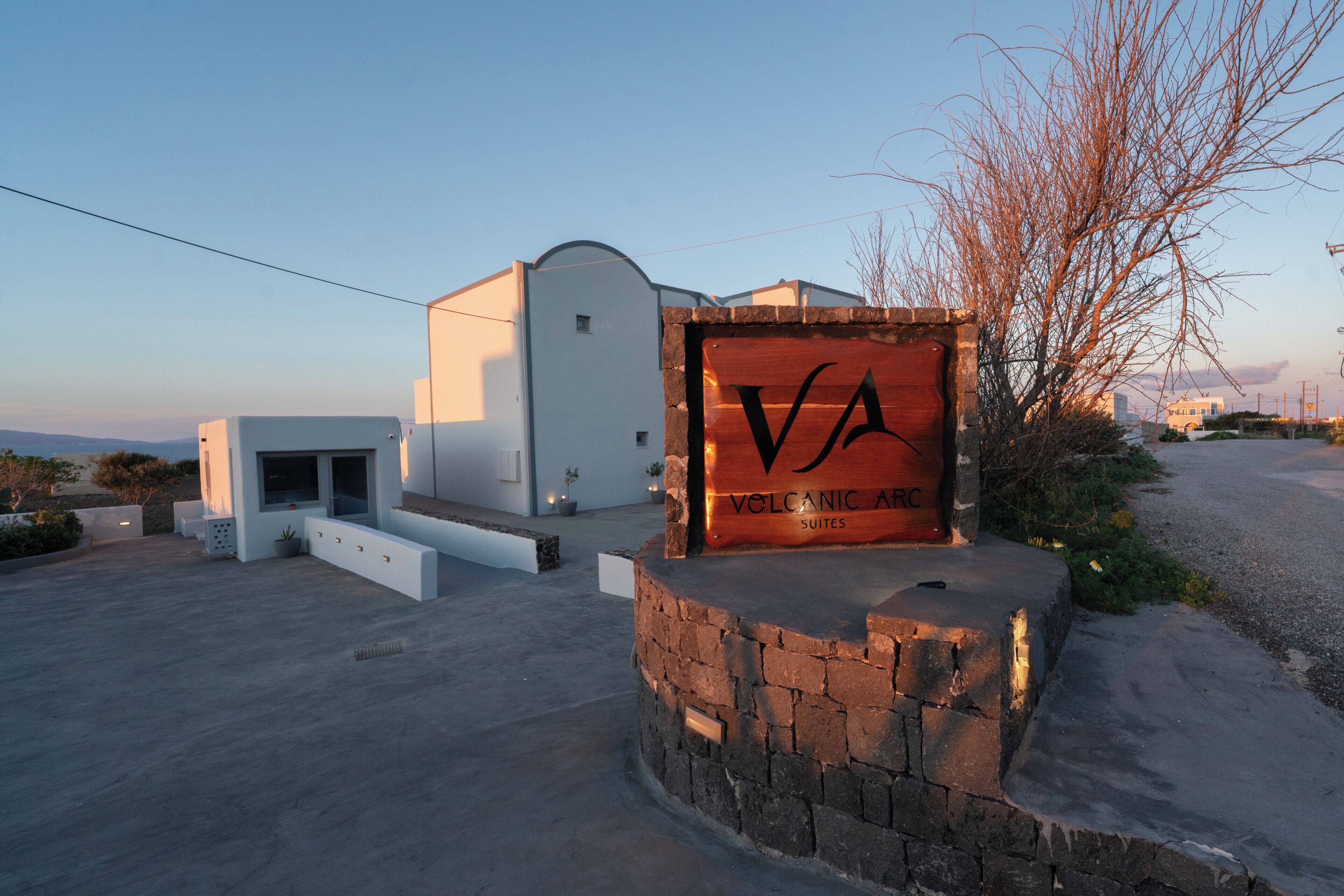 A building with a sign reading 'VOLCANIC ARC SUITES' and a stone wall.