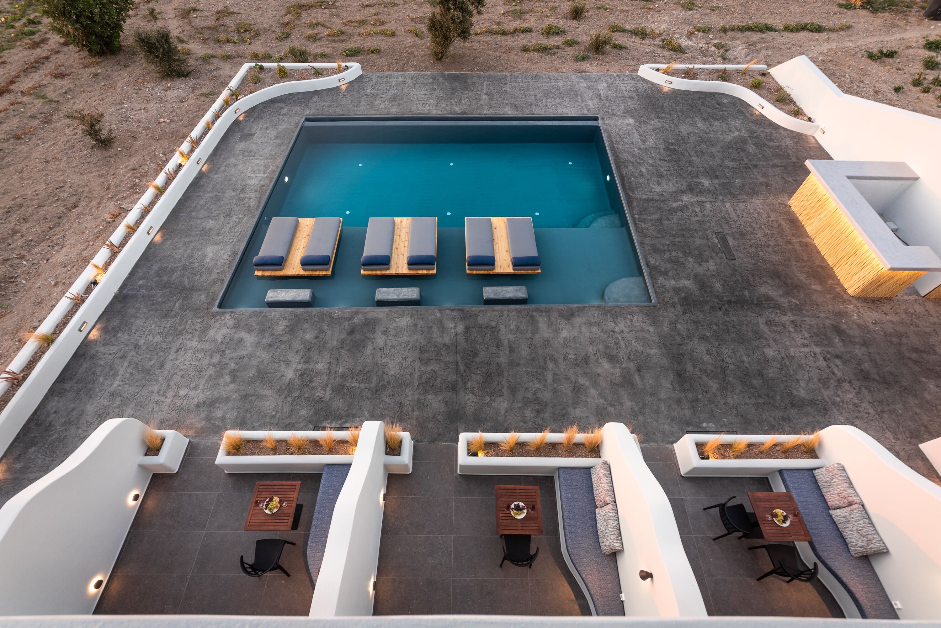 Une piscine sur le toit, dotée de chaises longues et d’une table, entourée de jardinières blanches et d’espaces de détente.