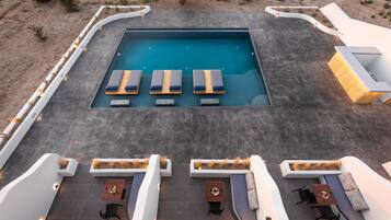 Une piscine sur le toit, dotée de chaises longues et d’une table, entourée de jardinières blanches et d’espaces de détente.