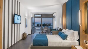 A modern hotel room with a large bed, a seating area with a view, and a television on the wall. - Volcanic Arc Suites (Santorini)