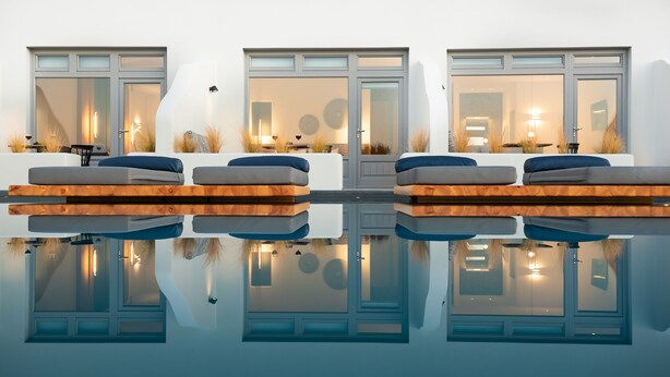 A modern outdoor seating area with cushioned benches and a reflective pool. - Volcanic Arc Suites (Santorini)