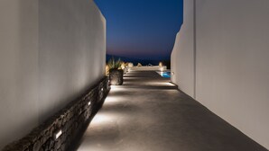 A corridor with a pool at the end, surrounded by white walls and stone accents. - Volcanic Arc Suites (Santorini)