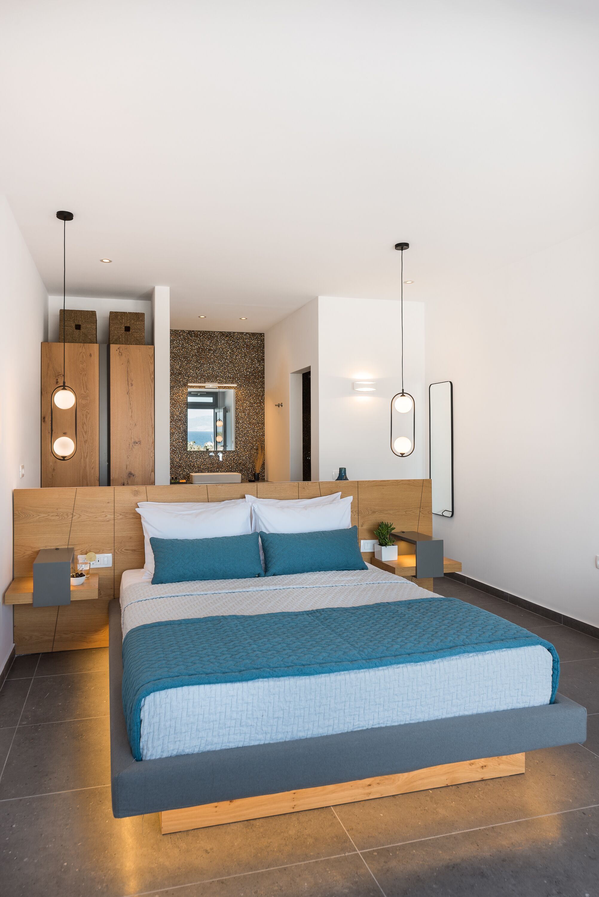 A modern bedroom with a large bed, wooden headboard, bedside tables, and a mirror.