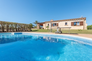 A swimming pool with a tiled edge, a building with a tiled roof, and a pergola with a table and chairs. - Fantastic Country Estate with Pool, Garden, Terrace, Air Conditioning and Wi-Fi (Artá)