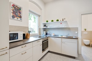 Une cuisine moderne avec des meubles blancs, un four à micro-ondes, un four traditionnel, un évier et une fenêtre.