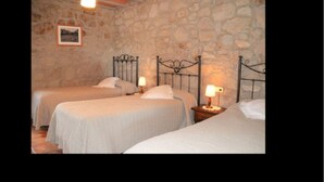 Una habitación con tres camas frente a una pared de piedra, cada una con una mesita de noche y lámpara.