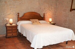 Un dormitorio con una cama de madera, dos mesitas de noche con lámparas y una pared de piedra.