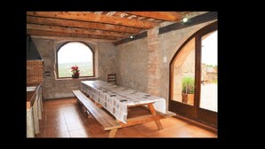 Un comedor rústico con una mesa larga, bancos y vistas a través de un amplio ventanal arqueado.
