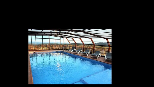 Una piscina interior con paredes de vidrio transparente, sillas de descanso y vistas a un paisaje boscoso.