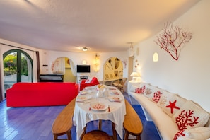 A dining area with a round table set for four, a red sofa, and a white couch with red decorative pillows.
