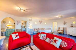 A spacious living area with red sofas, white walls, and a dining area.