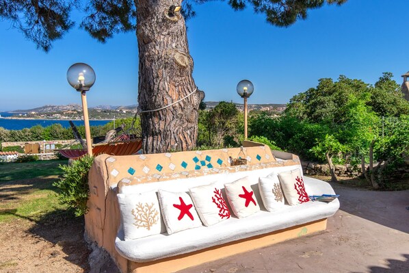 A bench with decorative cushions, a lamp post, and a view of the sea.