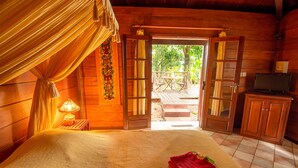 A wooden cabin room with a bed, a table, and a television. - Baobab Et Palmiers (L'Étang-Salé)