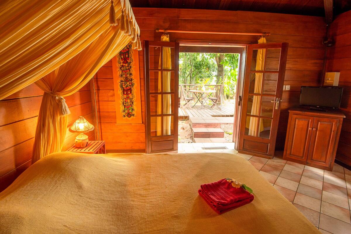A wooden cabin room with a bed, a table, and a television.