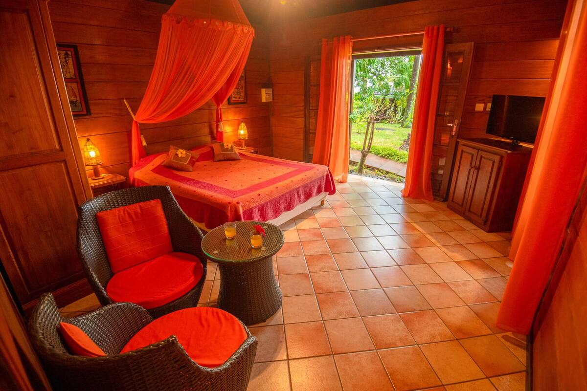A bedroom with a bed, a TV, wicker furniture, and a view of the outdoors.