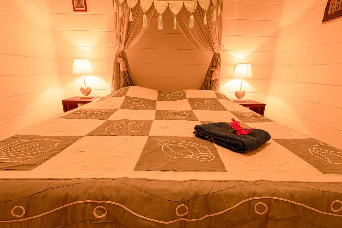 A bed with a checkered bedspread, a heart-shaped pillow, and a rolled towel with a flower.