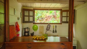 A kitchen with a window, wooden cabinets, a coffee maker, a colander, a banana bunch, and a hanging cloth. - Baobab Et Palmiers (L'Étang-Salé)