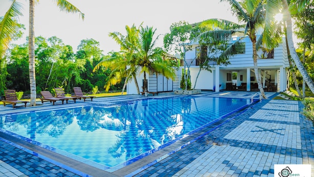 Piscina con sillones de descanso y palmeras, rodeada por un edificio con zona techada.