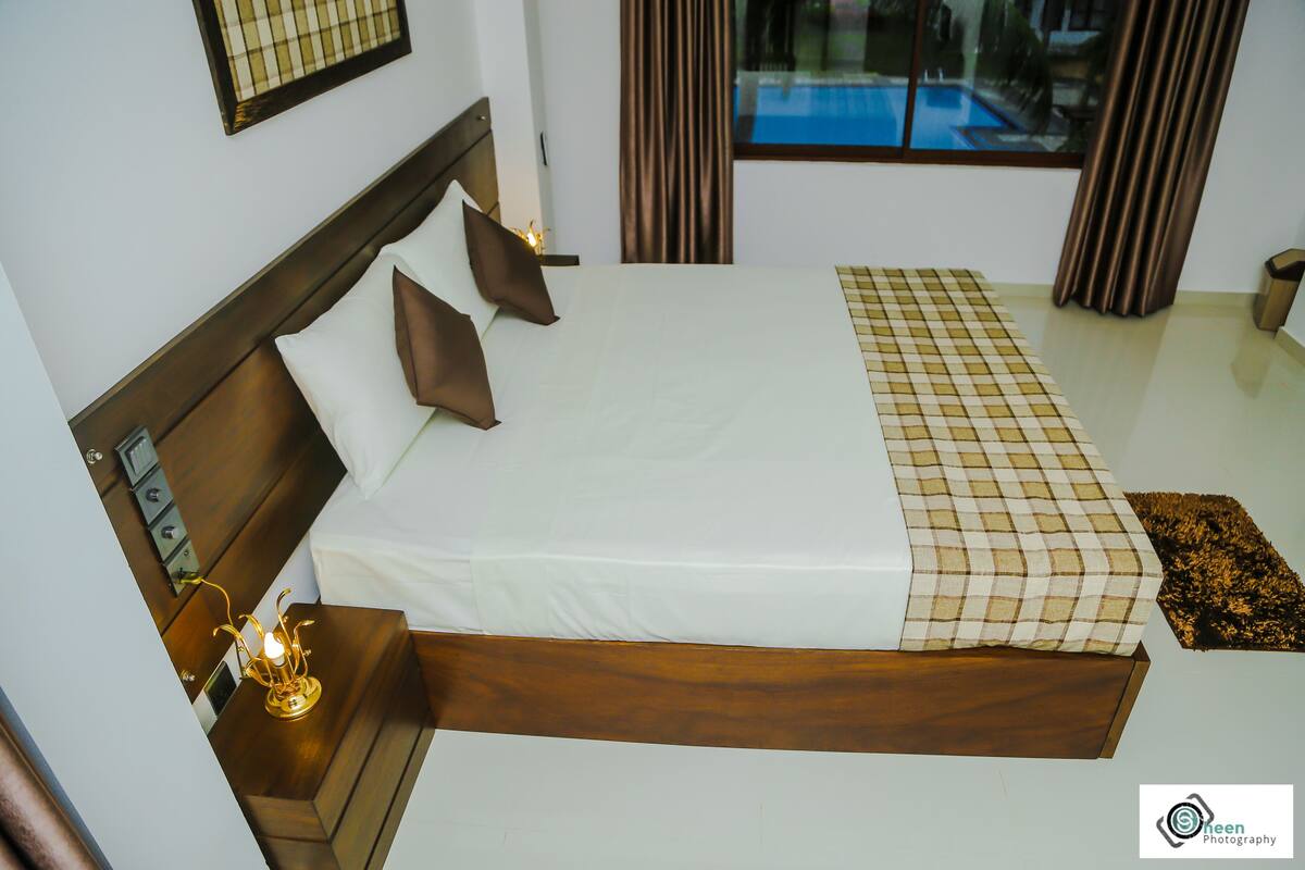A neatly made bed with a wooden headboard, a bedside table with a lamp, and a window with curtains.