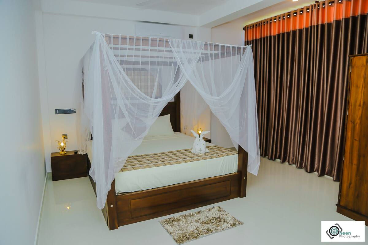 A bedroom with a canopy bed, a nightstand with a lamp, and a wooden wardrobe.