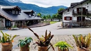 A mountain village with traditional buildings, a paved square, and potted plants in the foreground.