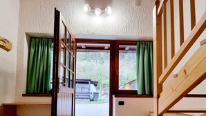 A room with a wooden staircase, a bench, a door leading outside, and a view of a parked vehicle.